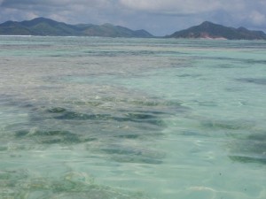 a clear blue water with mountains in the background