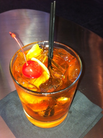 a glass of orange drink with ice and a cherry