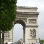 a large stone arch with statues and people walking by with Arc de Triomphe in the background