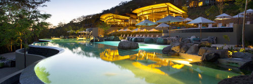 a pool with a building and a pool with umbrellas and chairs