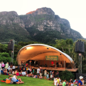 a group of people sitting on grass and a stage with a mountain in the background