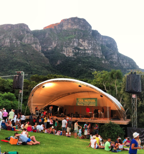 a group of people sitting on grass and a stage with a mountain in the background