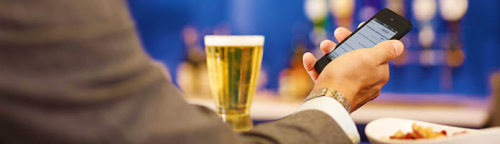 a person holding a cell phone and a glass of beer