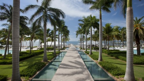 a long walkway with palm trees and a pool with Laie Hawaii Temple in the background