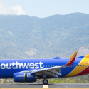 a blue and yellow airplane on a runway with mountains in the background