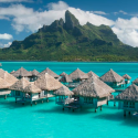 a group of huts in water with Bora Bora in the background