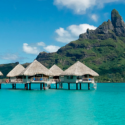 a group of huts on stilts in water with Bora Bora in the background