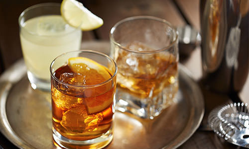 a glass of liquid with ice and a lemon on a tray