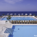 a pool with chairs and a beach in the background