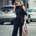 a woman in black outfit holding a jacket and looking at her phone