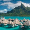 a group of huts on water with a mountain in the background