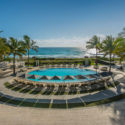 a pool with lounge chairs and palm trees by the ocean