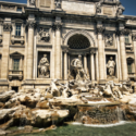 a stone building with statues in front of it with Trevi Fountain in the background