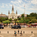 a group of people walking on a street with a large building in the background with Jackson Square in the background