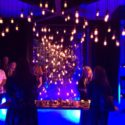 a group of people standing around a table with lights from the ceiling