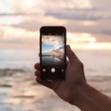 a hand holding a phone with a sunset in the background