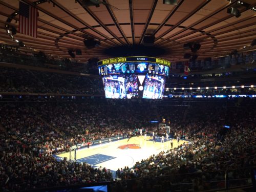 a basketball game in a stadium with Madison Square Garden in the background