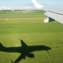 an airplane wing and shadow of a plane on a green field