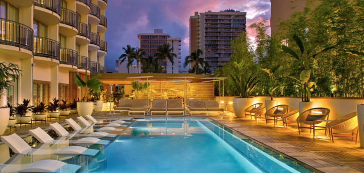 a pool with chairs and trees in front of buildings