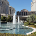 a water fountains in a pool with a large building in the background with Caesars Palace in the background