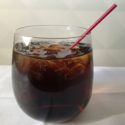 a glass of brown liquid with ice and a straw