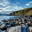 a rocky beach with a body of water and mountains in the background