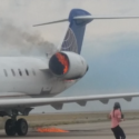a woman walking on a runway with a jet engine on fire