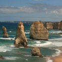 a large rock formations on a beach with The Twelve Apostles in the background