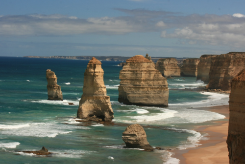 a large rock formations on a beach with The Twelve Apostles in the background