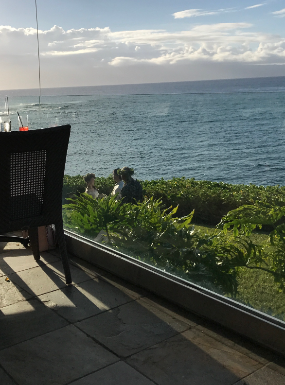 a group of people sitting outside by a window overlooking the ocean