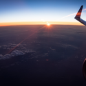 an airplane wing and the sun above the clouds