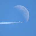 a plane flying in the sky with the moon behind it