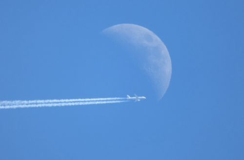 a plane flying in the sky with the moon behind it