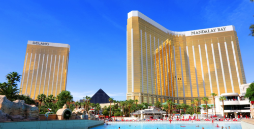 a large gold building with a pool and people swimming in it with Mandalay Bay in the background
