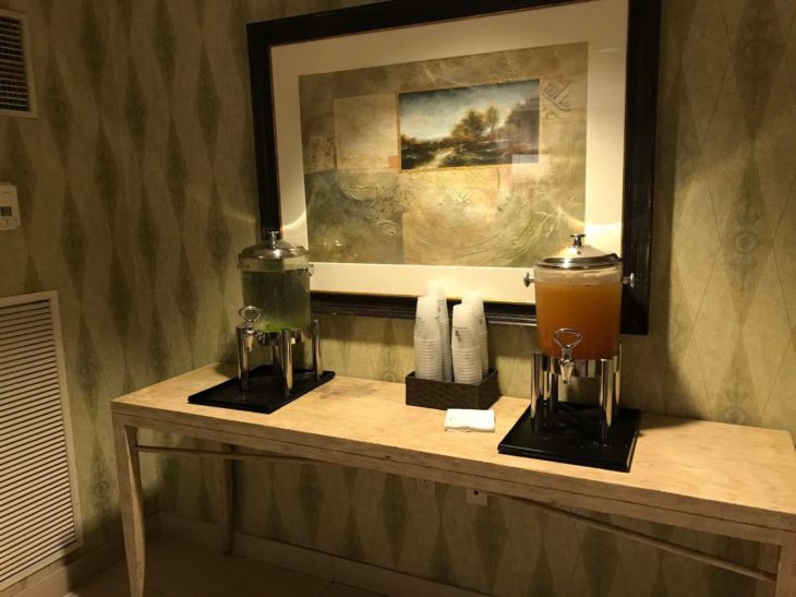 a table with a drink dispenser and a painting on the wall