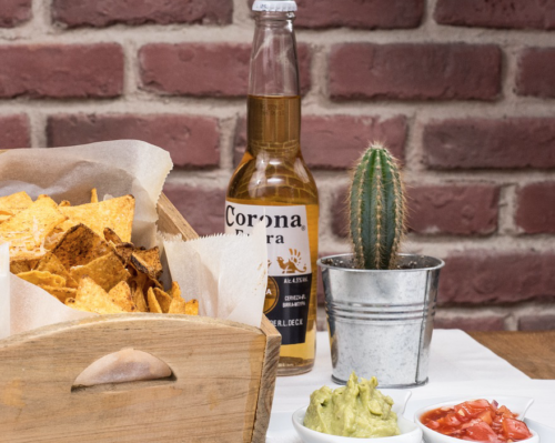 a bowl of chips and a cactus next to a bottle of beer