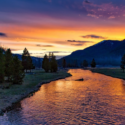 a river running through a valley with trees and mountains in the background