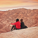 two women sitting on a hill looking at a mountain