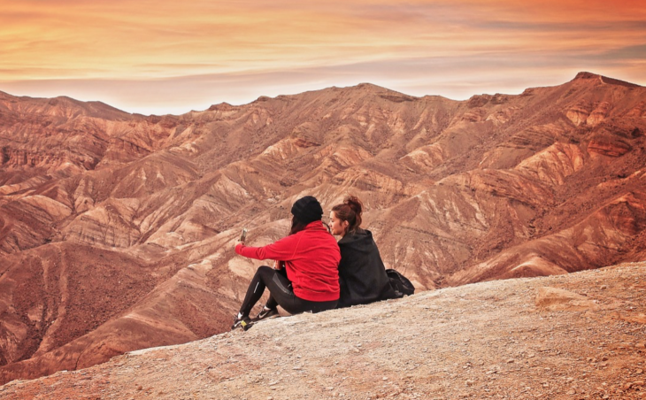 two women sitting on a hill looking at a mountain