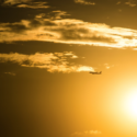 a plane flying in the sky with the sun behind it