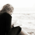 a woman sitting on the beach reading a book