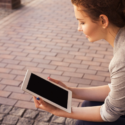 a woman sitting on a brick sidewalk holding a tablet
