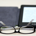 a pair of glasses next to a kindle