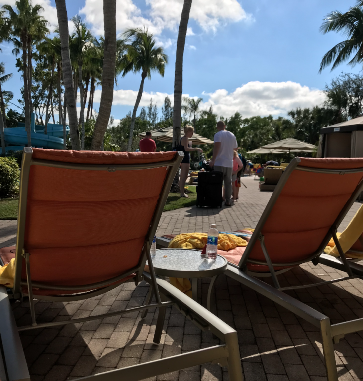 chairs on a brick patio with palm trees and people in the background