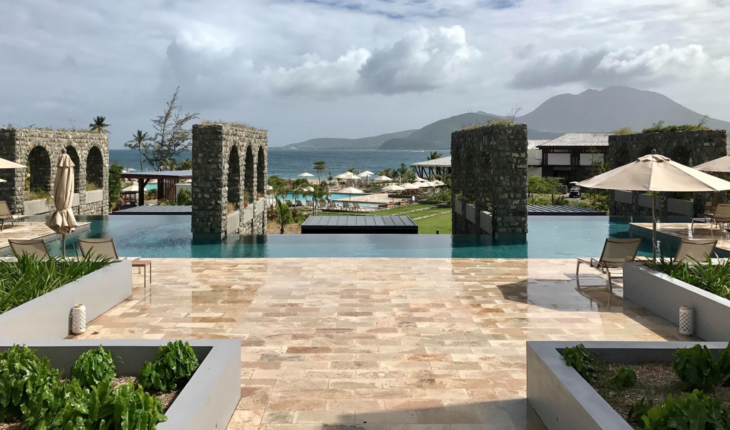 a pool with stone pillars and a beach and mountains in the background