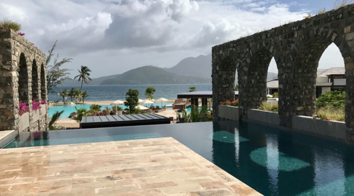 a pool with a stone arch over it and a beach in the background