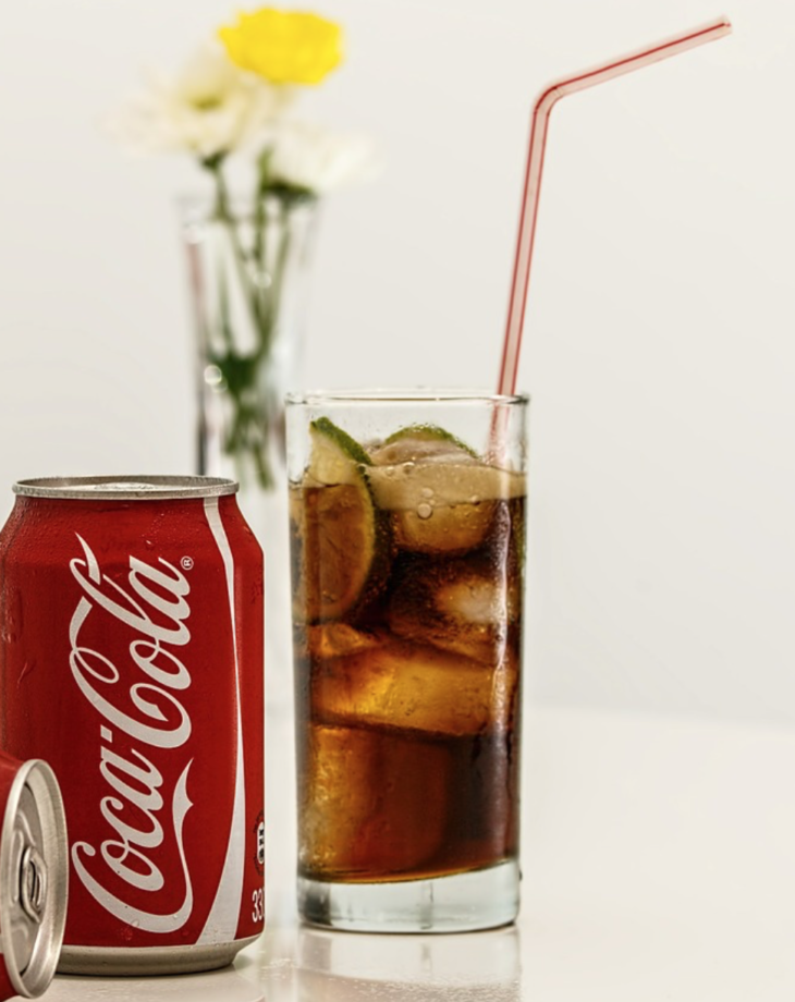 a can of soda and a glass with ice and a straw