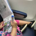 a child sitting on a plane with a book and a marker