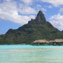 a group of bungalows in the water with Bora Bora in the background