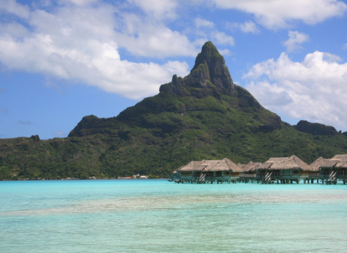 a group of bungalows in the water with Bora Bora in the background